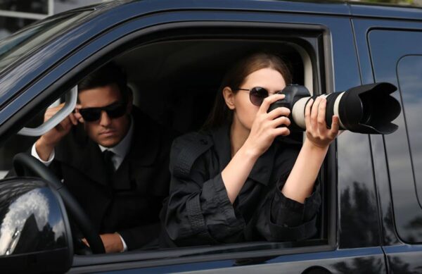 detektyw siedzi w samochodzie obok kobiety detektyw która robi zdjęcie aparatem