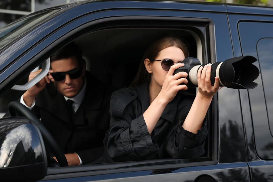detektyw siedzi w samochodzie obok kobiety detektyw która robi zdjęcie aparatem
